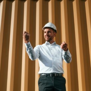 Standing against yellow background. Male worker is on the location with containers